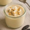 Verrine de crème dessert à la fève tonka avec morceaux de nougat, posée sur une serviette beige avec fèves tonka en décor